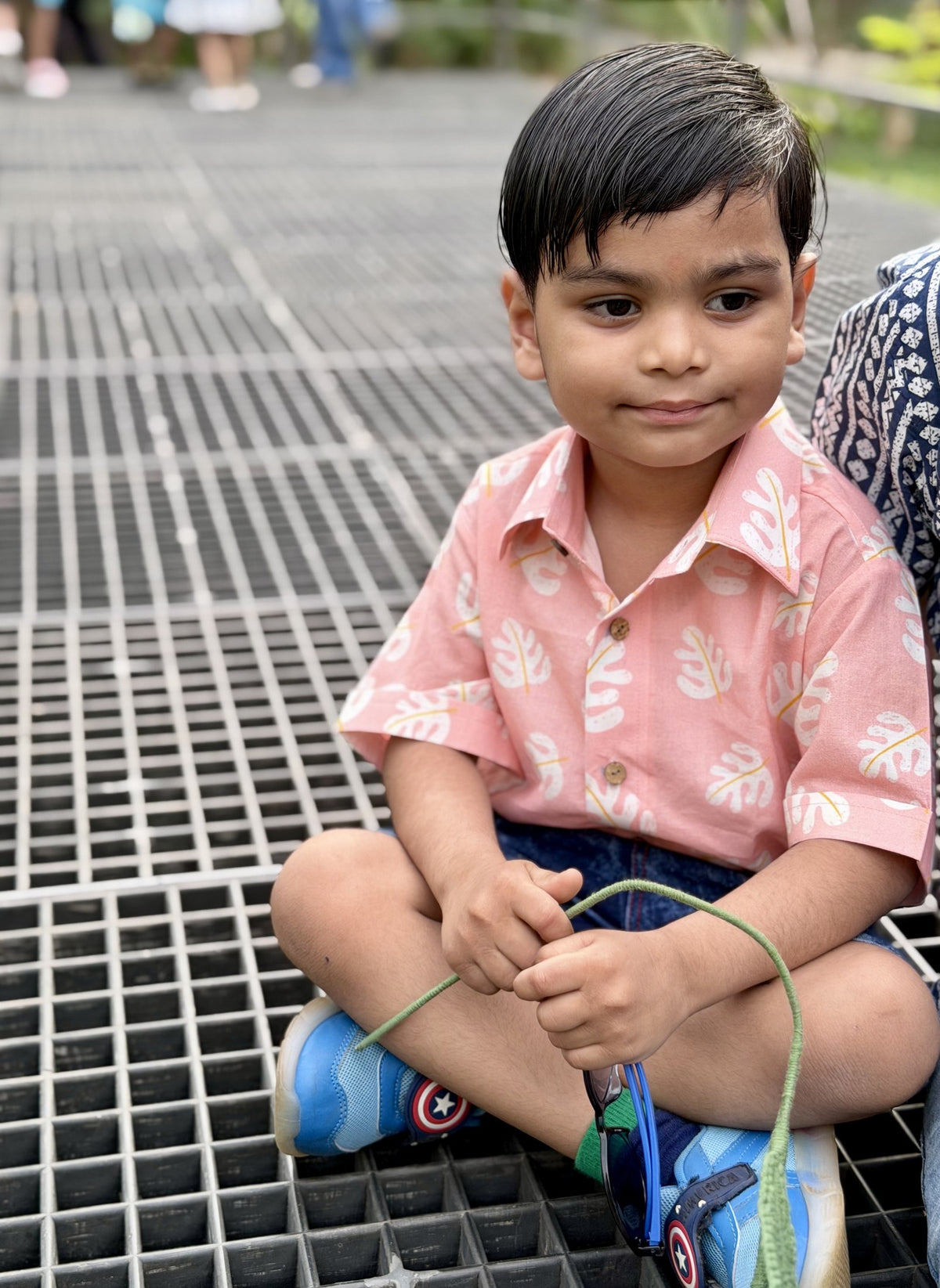 Boy sitting in Basic Tribe Barfi peach printed collared shirt, close-up view
