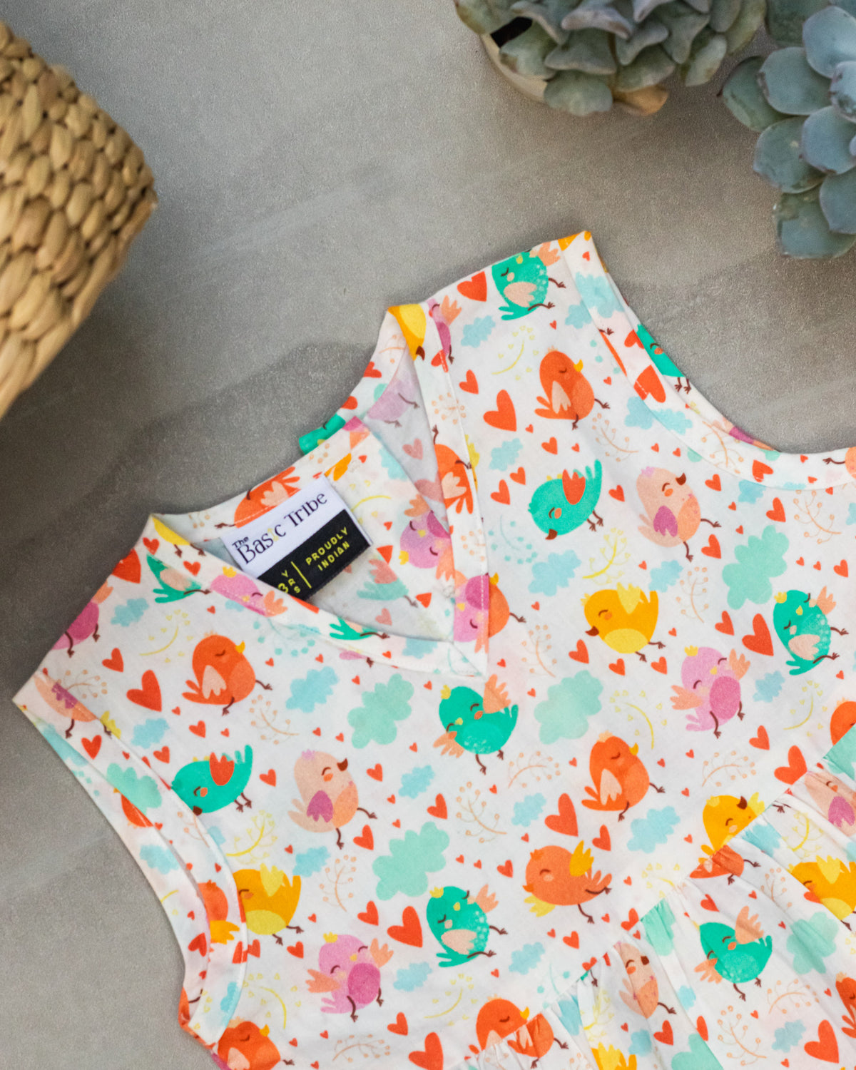 Flat lay detail of Basic Tribe Twitter dress showing colourful bird-print fabric and neckline